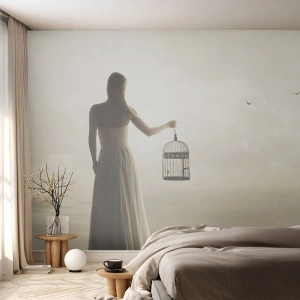 Fotobehang Standard Eco - Een vrouw met een kooi kijkt in de verte tegen de lucht en de zee in - 100x70cm - Wees vrij - Moderne wanddecoratie voor woonkamer en slaapkamer ARTTOR