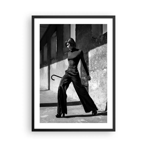 Poster in een zwarte lijst - Een vrouw in een elegante outfit met een wandelstok tegen de achtergrond van sobere architectuur - 50x70cm -   Stedelijke elegantie - Moderne wanddecoratie voor woonkamer en slaapkamer ARTTOR